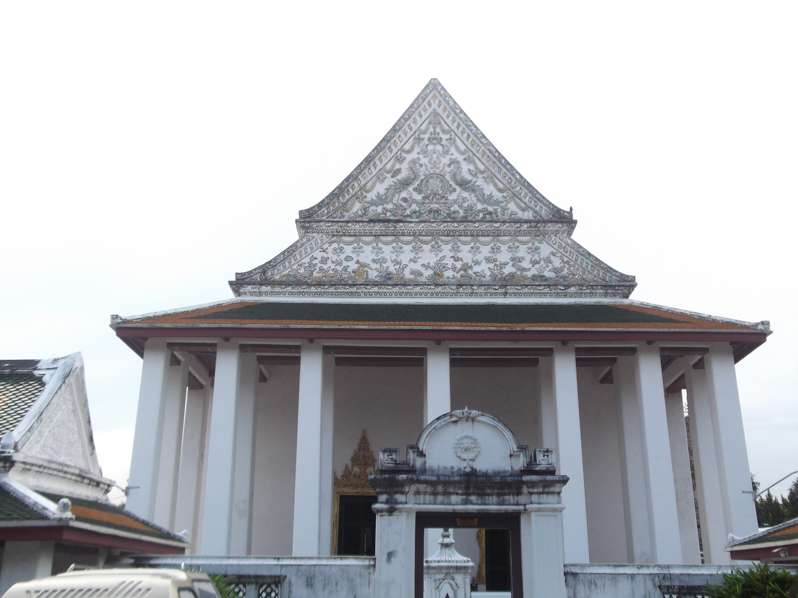 Wat Thepthidaram戒堂白色高柱与密集彩色花纹山墙，前方矮墙有拱门