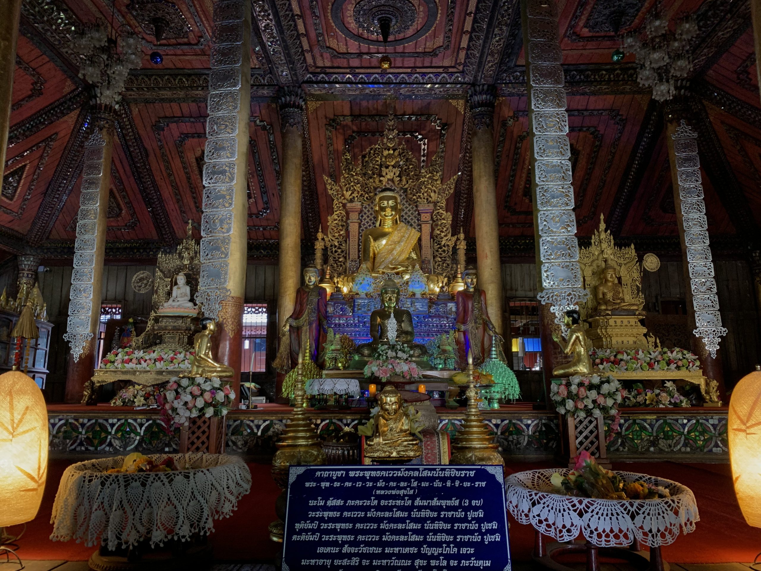 Nantaram 金色佛坛上方的红褐木板天花、圆形镜饰与柱间银白悬饰
