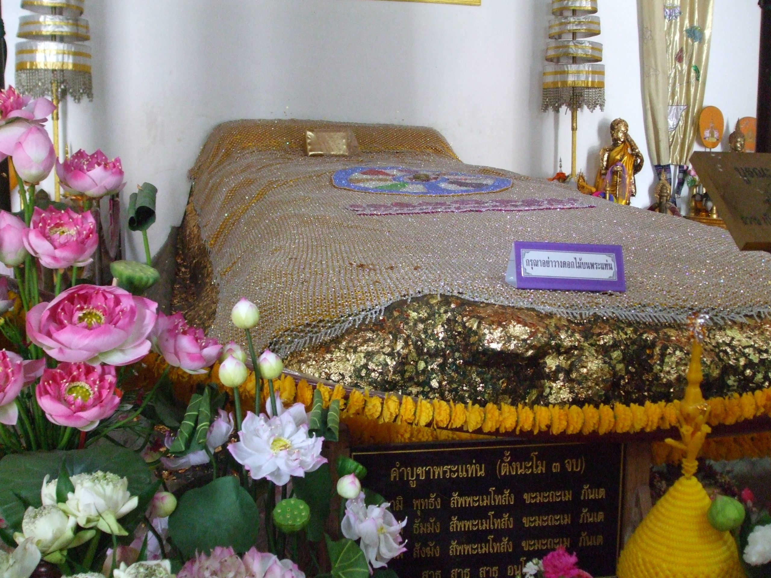 2012年北碧Phra Thaen Dong Rang石卧座，银白网状覆饰、金色不规则岩边、黄色花串与左侧粉莲花，右侧紫框请勿放花牌